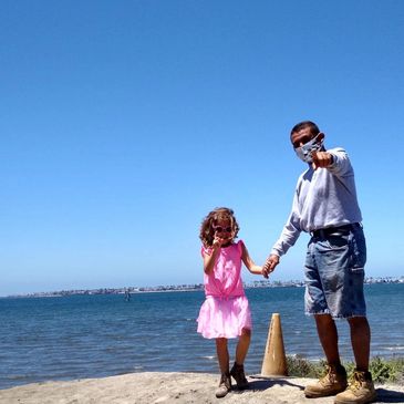 Man and little girl holding hands by the water on a sunny day.