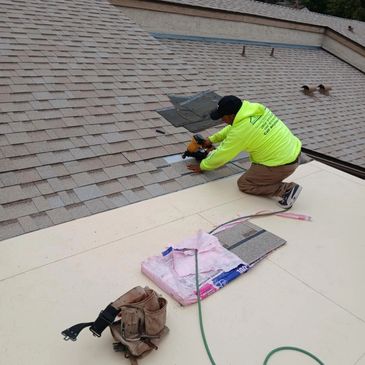 A worker installing shingles on a roof with tools nearby.