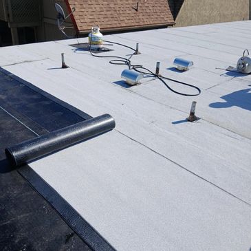 A white flat roof with ventilation pipes and a propane tank under sunny weather.