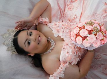 Young woman in a pink dress and tiara lying down with a bouquet.