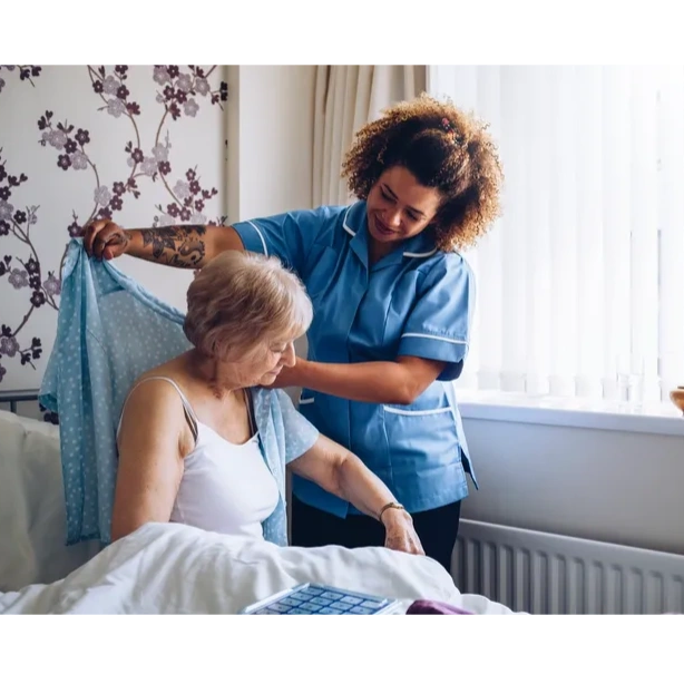 A homecare assistant helping an older woman get dressed and out of bed.
