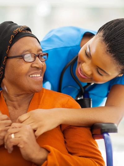 A homecare person assisting an elderly woman who is in a wheelchair.