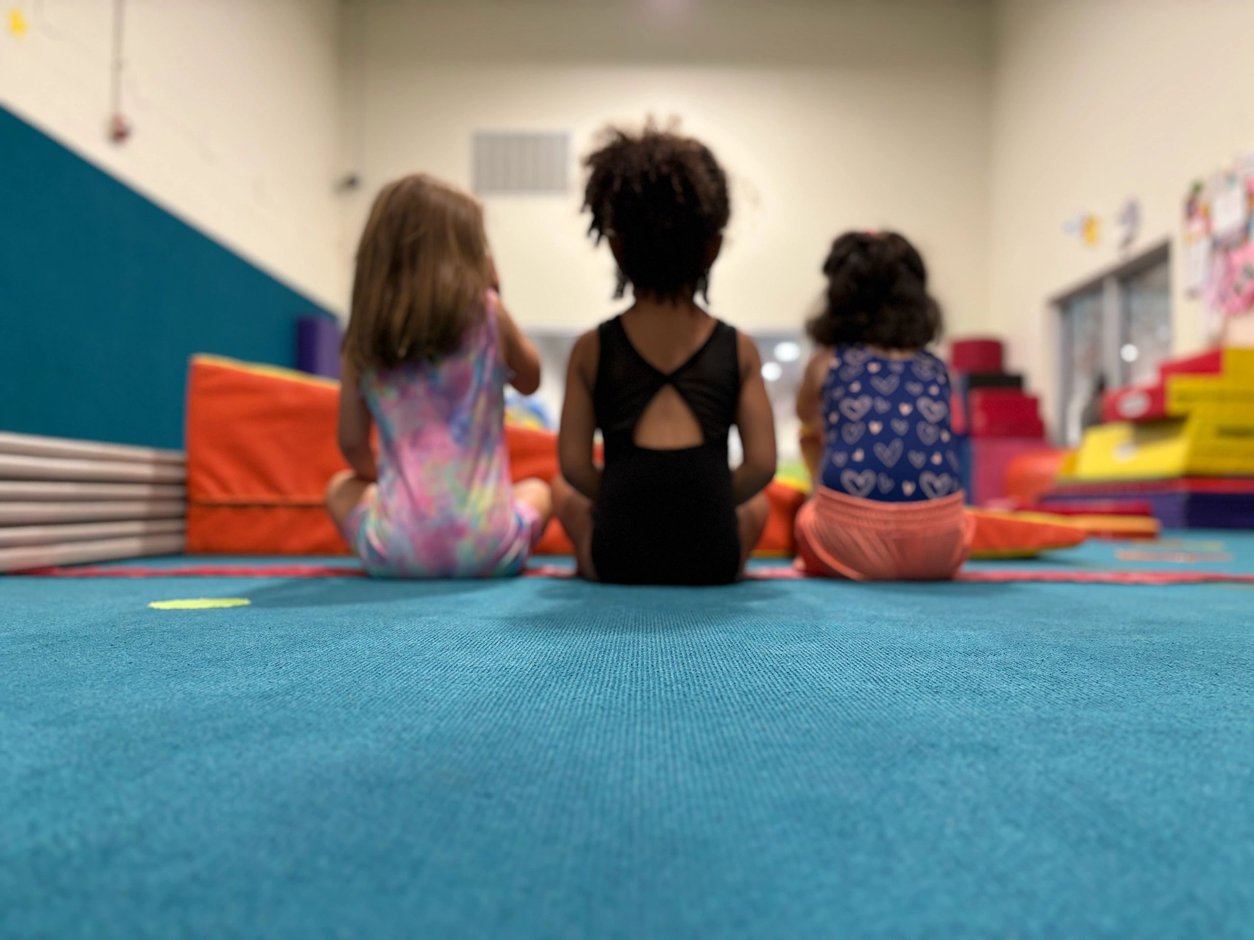 Three children sitting on a blue mat facing forward.