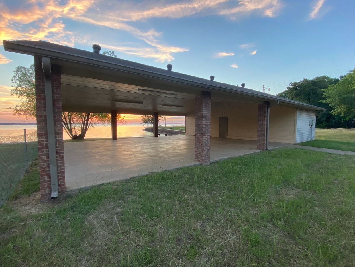 Open pavilion by the lake at sunset with a grassy foreground.