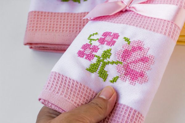 Hand holding a pink towel with embroidered flowers and a ribbon.