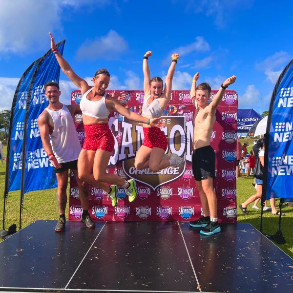 Four young adults celebrating at a Samson Challenge event on a sunny day.