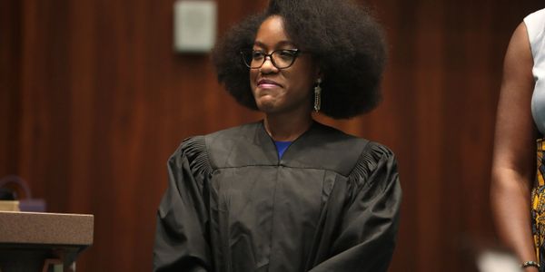 Woman in a black judge's robe standing with a confident smile.