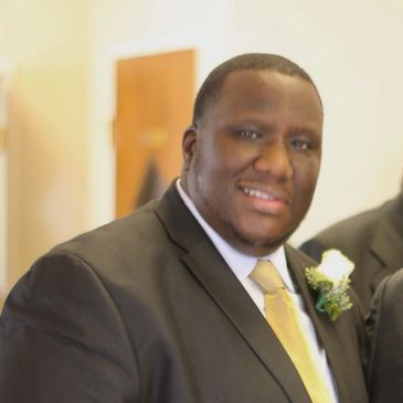 Man in a suit with a yellow tie smiling at a formal event.