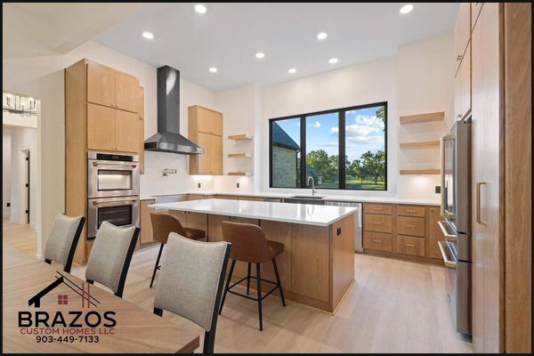 Modern kitchen with wooden cabinets, a large island, and a view of the outdoors through a big window.