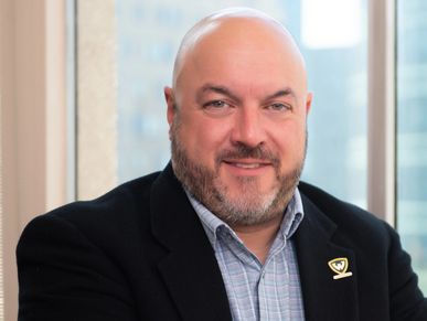 Professional portrait of a bald man with a beard in a suit jacket.