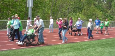 Group of people walking and using mobility aids on a track outdoors.