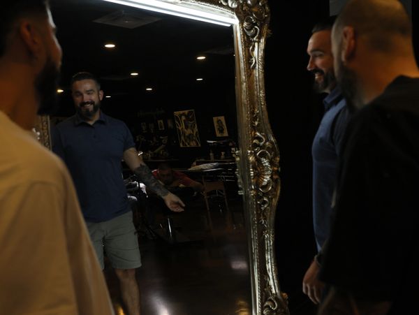 Three men smiling and looking at a large ornate mirror with lights.