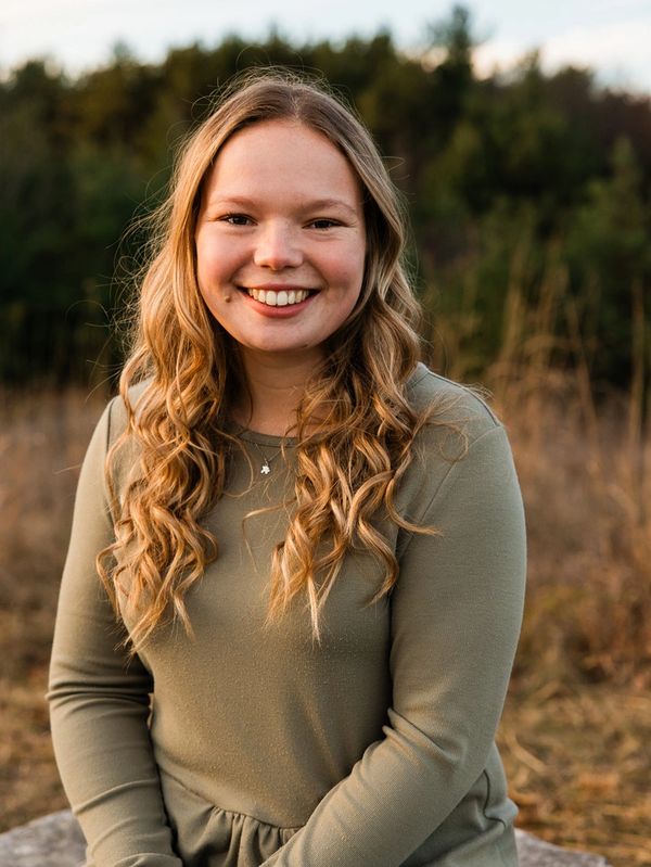 Young woman with long curly hair smiling outdoors in a natural setting.