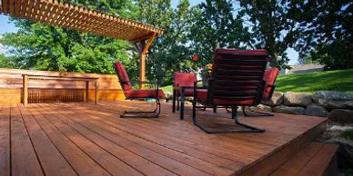Spacious wooden deck with outdoor seating and a pergola in a lush backyard.