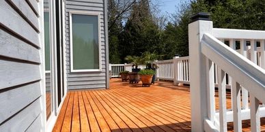 Spacious wooden deck attached to a house with white railing and potted plants.