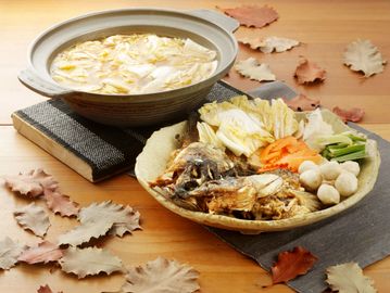 A hot pot meal with fresh vegetables, fish, and mushrooms on a wooden table.
