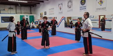 Martial arts class practicing with swords in a spacious dojo.
