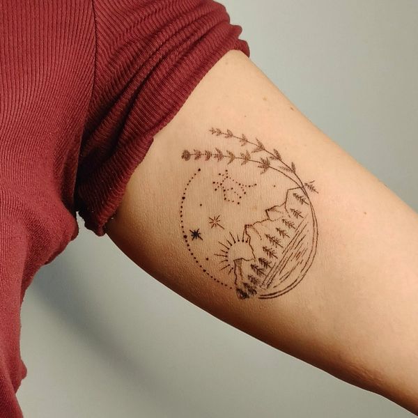 Minimalist tattoo of a mountain landscape with sun, stars, and floral elements on an arm.
