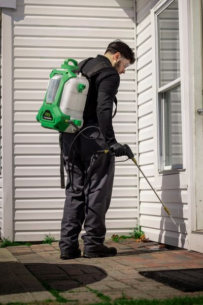 Man spraying pesticide on a house exterior with protective gear.