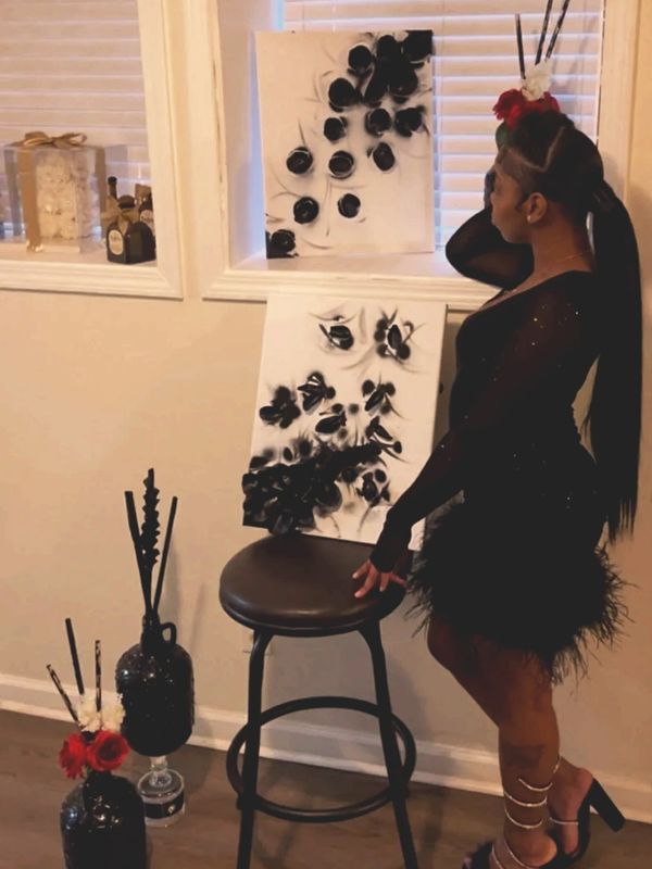 Woman in black dress posing with abstract black and white art and floral decor.
