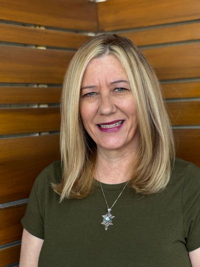 Smiling woman with blonde hair standing against a wooden slat wall.