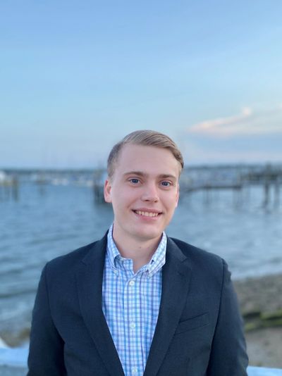 Young man in a blazer smiling by the waterfront at dusk.