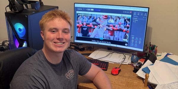 Young man smiling at desk with computer setup.