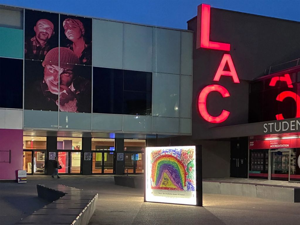 Night view of a building with red 'LAC' letters and a rainbow display.