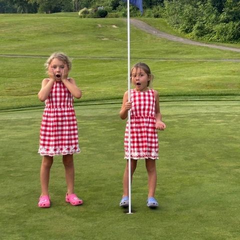 two small girls on a golf green with flagstick