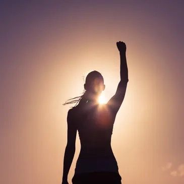 Silhouette of woman with arm raised against background of the sun