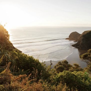 Sunlit coastal landscape with waves and rocky cliffs.