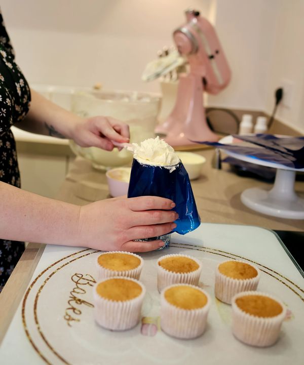 Person decorating cupcakes with frosting using a piping bag.