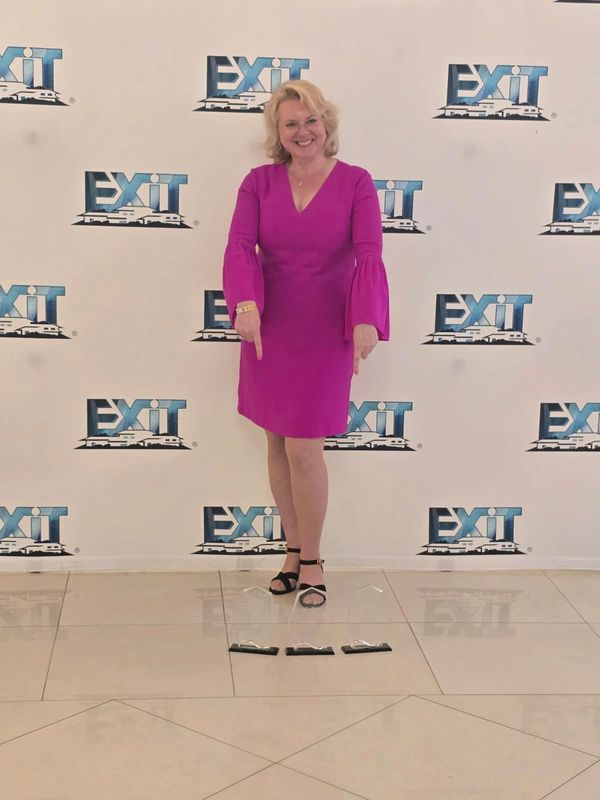 Smiling woman in a magenta dress points down at three wrapped items on the floor.