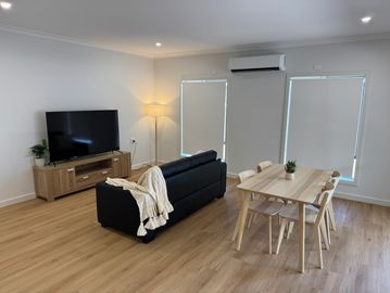Minimalist living room with black sofa, wooden dining set, and TV on a wooden stand.