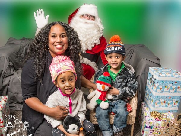 Family with two kids posing with Santa Claus beside wrapped Christmas presents.