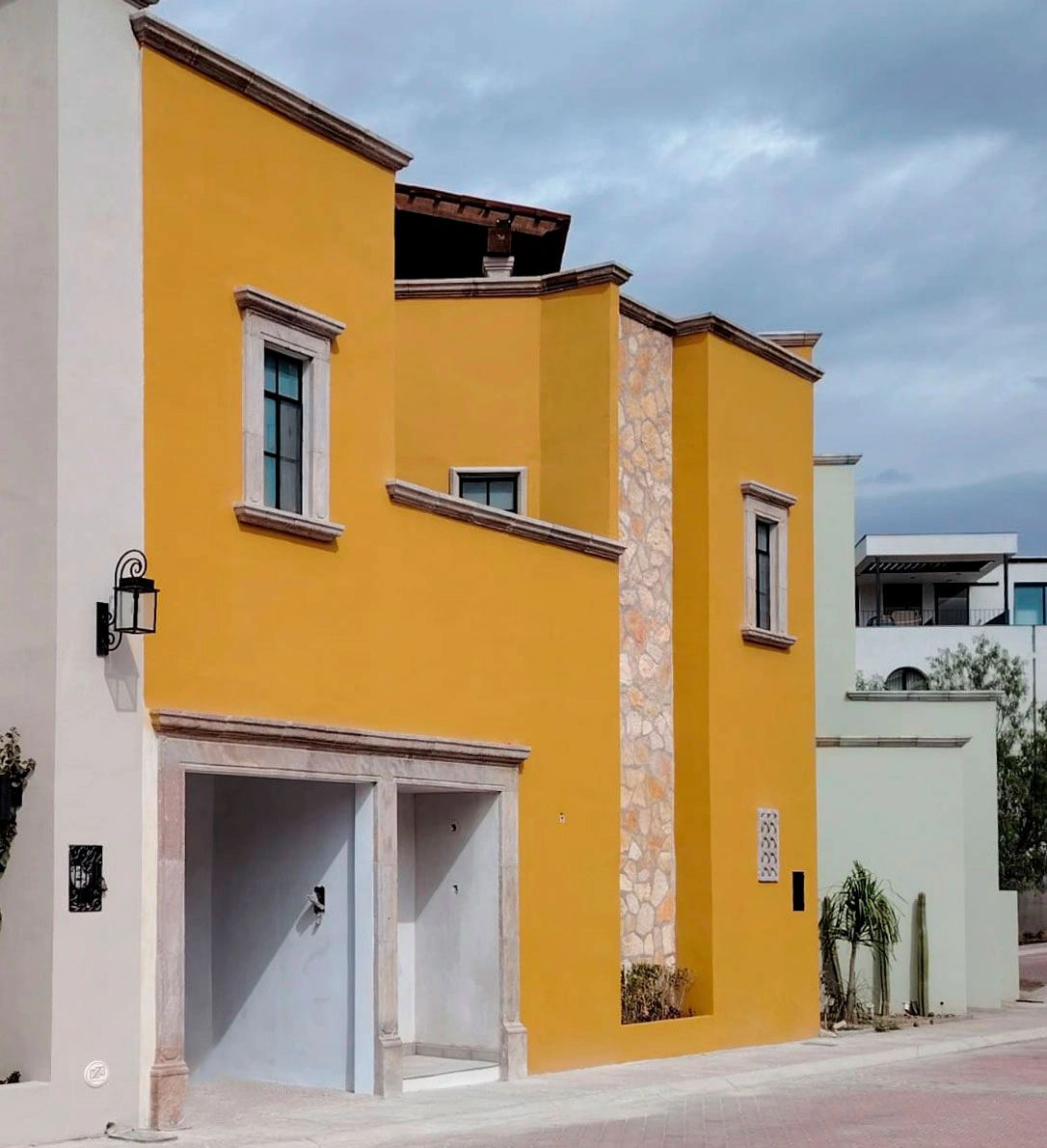 Villa Tamayo, fachada color amarillo con muro de piedra y ventanas con marcos de cantera.