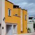 Villa Tamayo, fachada color amarillo con muro de piedra y ventanas con marcos de cantera.