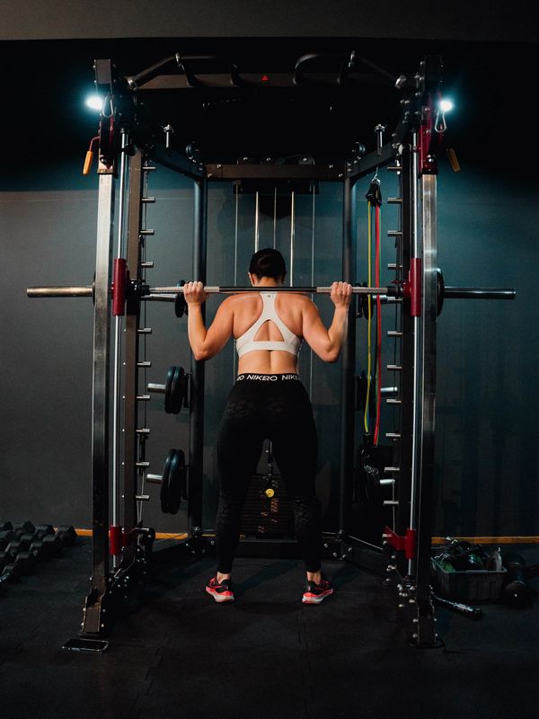 Mujer haciendo sentadillas con barra en gimnasio.