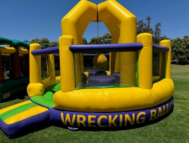 Inflatable wrecking ball game in bright yellow and green on grass.