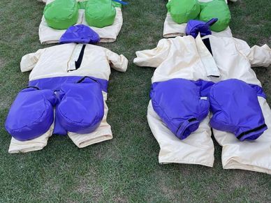 Two inflatable sumo wrestler costumes laid out on grass.