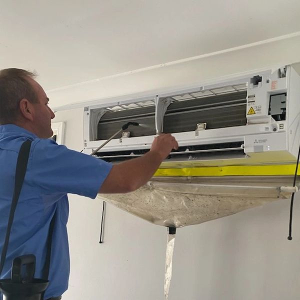 Technician cleaning an air conditioner with a spray tool and protective cover.