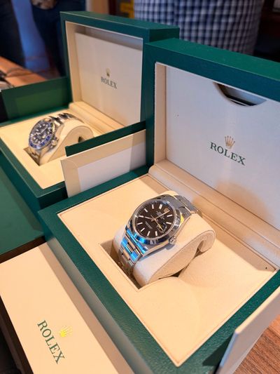Two Rolex watches displayed in open green boxes on a table.