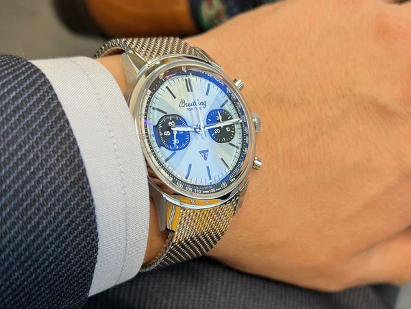Luxury Breitling Top Time watch with mesh strap on a well-dressed wrist.