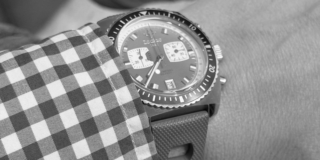 Close-up of a wristwatch partially covered by a checkered shirt sleeve.
