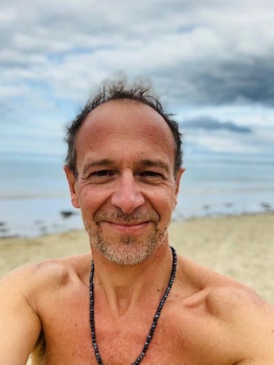 Smiling man with a beard at the beach under cloudy skies.