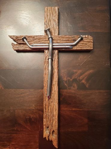 Cross made of weathered wood and bent nails arranged on a wooden surface.