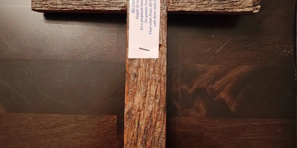 Rustic wooden cross with a small paper note attached, placed on a dark wooden surface.