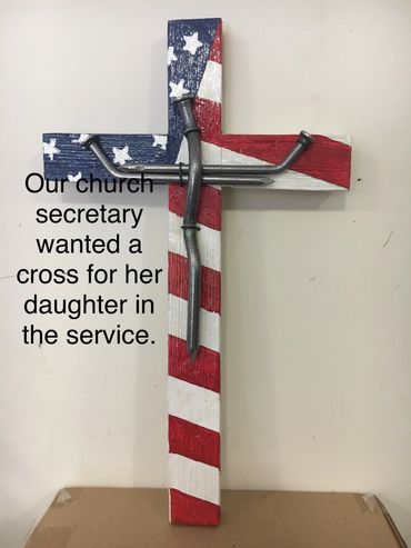 A patriotic wooden cross with nails forming Jesus' figure and a text about a church secretary.