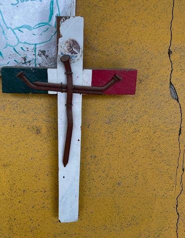 Rusty nails form a cross on a painted Mexican flag background against a yellow wall.