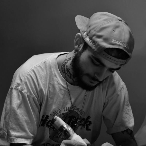 Black and white portrait of a tattooed man wearing a cap backward.